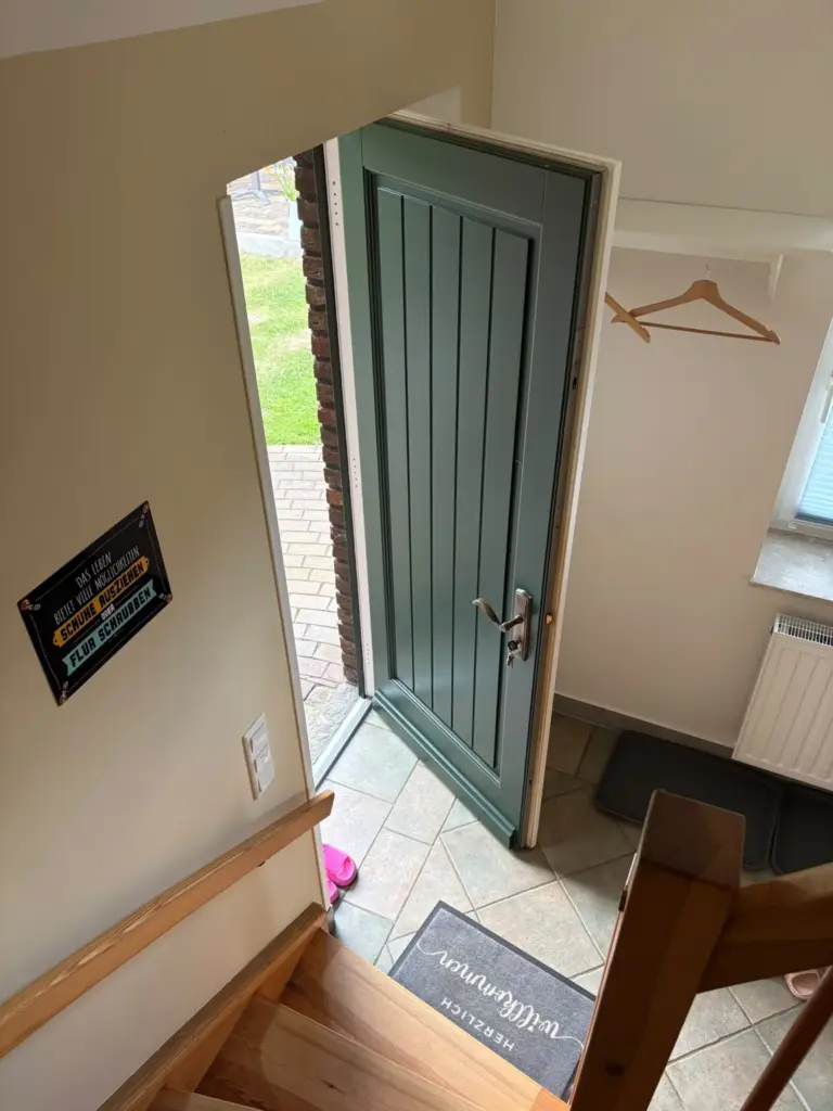 Blick von der Treppe auf die gruene Eingangstuer mit Fussmatte