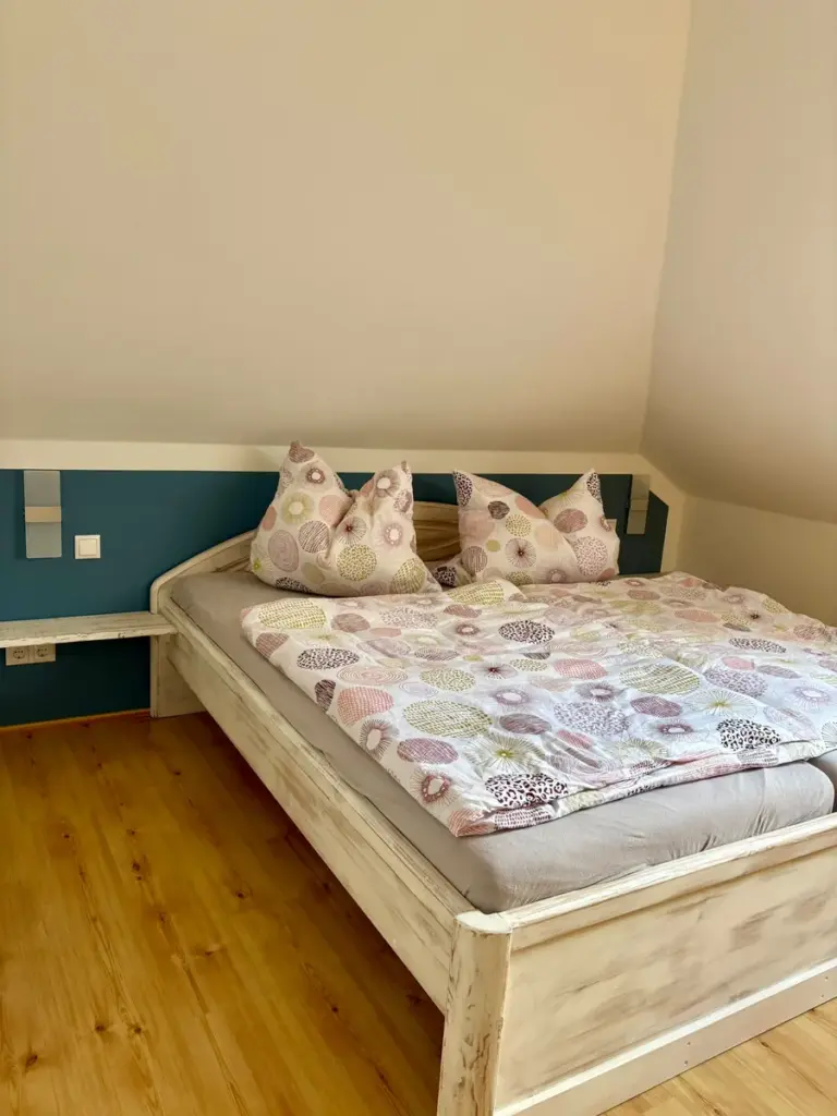 Doppelbett mit gemustertem Bettbezug vor petrolfarbener Wand
