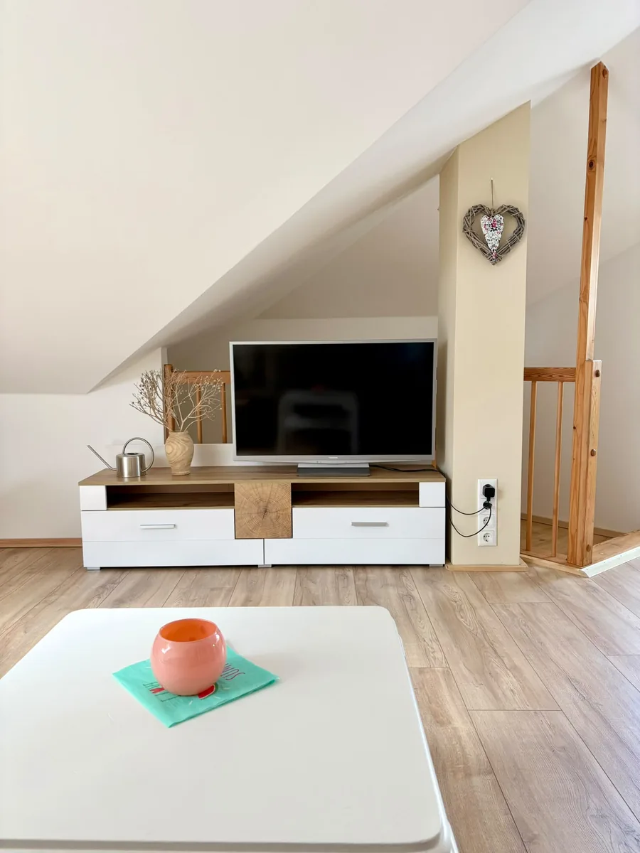 Sideboard mit Fernseher unter der Dachschräge, darüber ein Herz aus Weidengeflecht