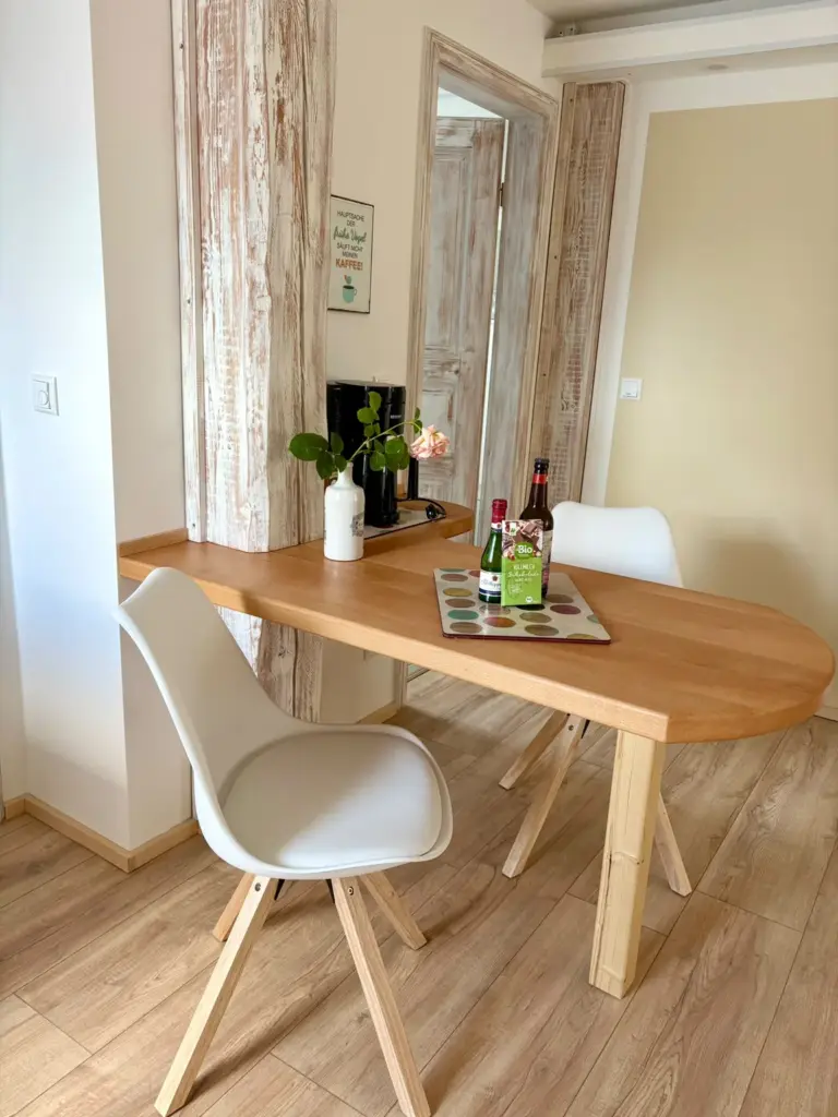 Ovaler Esstisch mit zwei hellen Schalenstühlen und einer Rose in der Vase im Innen-Essbereich